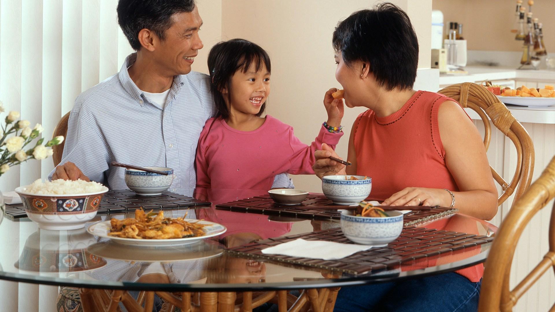 A parent and two children getting ready together at a kitchen table in the morning light